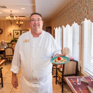A chef holding a plated dish in a restaurant setting.