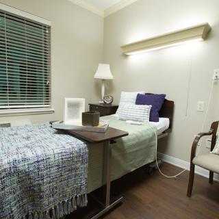 A hospital room with a single bed, bedside table, and chair.