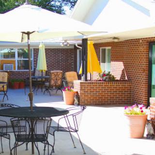 A cozy patio area with outdoor seating, umbrellas, and potted plants against a brick building.