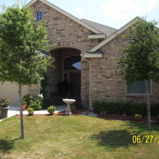 A front view of a brick house with a landscaped yard and trees.