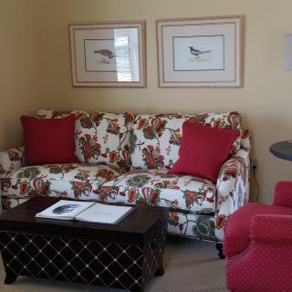 A cozy living room with a floral-patterned sofa, red armchair, and framed bird artwork on the wall.