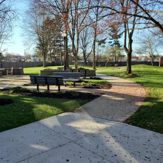 A serene park area featuring pathways, benches, and trees under a clear sky.