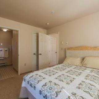 A cozy bedroom with a neatly made bed and an open door leading to another room.