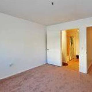 An empty room with carpeted flooring and white walls, featuring a doorway leading to another area.