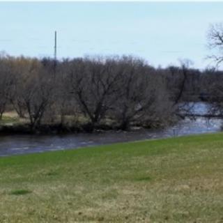 A serene landscape featuring a flowing river bordered by trees and grassy fields.
