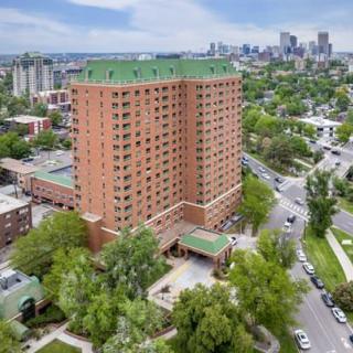 Aerial view of a tall brick apartment building surrounded by trees and roads, set against an urban cityscape.