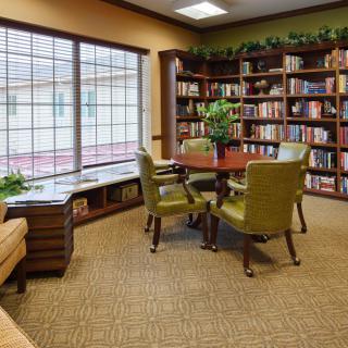 A cozy reading area in a library with bookshelves, chairs, and large windows.