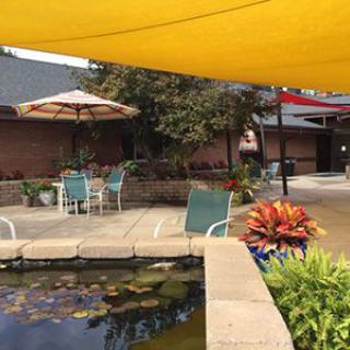 A tranquil courtyard with a pond, outdoor seating, and large shade sails overhead.