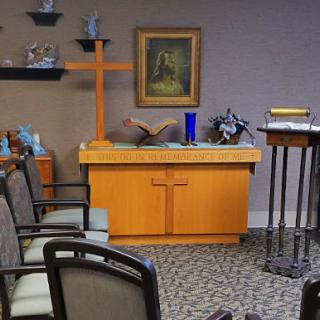 A serene chapel interior featuring an altar with a cross and seating for visitors.
