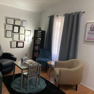 A cozy living room with a sofa, armchair, and coffee table, adorned with wall art and curtains.