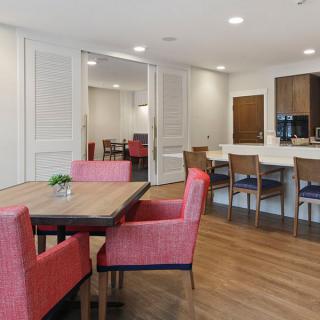 A modern dining area with a wooden table and pink upholstered chairs, adjacent to a kitchen with bar stools.