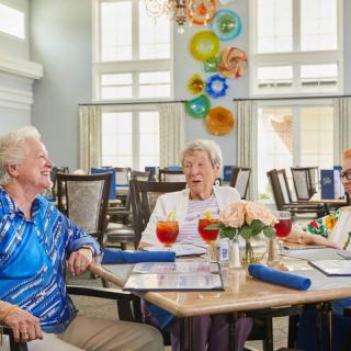 A group of seniors enjoying conversation and drinks in a dining setting.