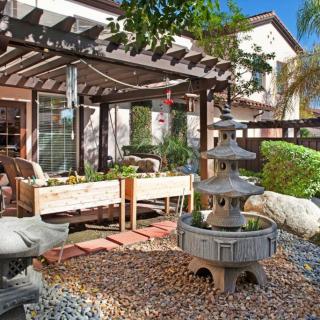 A serene outdoor patio featuring a pergola, zen-style fountain, and lush landscaping.