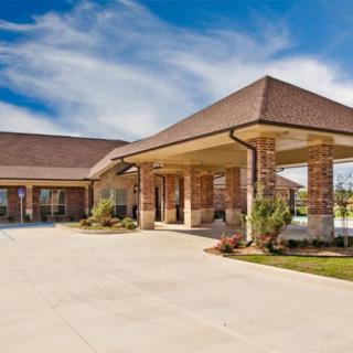 A modern building with a covered entrance and landscaped surroundings under a blue sky with clouds.