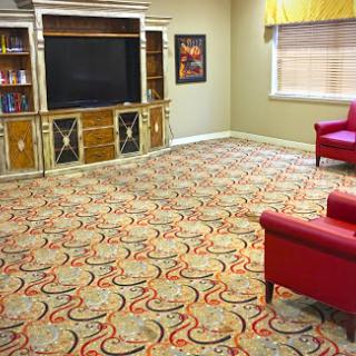 A cozy living room featuring a red chair, a large television, and an intricately patterned carpet.