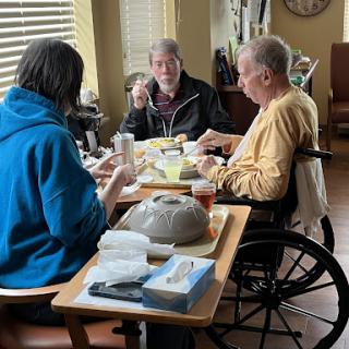 A group of three individuals enjoying a meal together, including one person in a wheelchair.