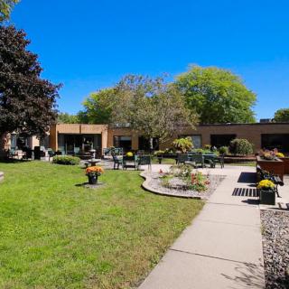 A peaceful garden with a patio and surrounding trees under a clear blue sky.