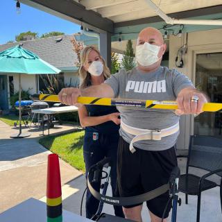 A person engaged in an outdoor physical therapy session with a therapist, both wearing masks.