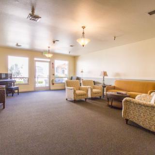 A spacious living room with comfortable seating, featuring sofas and armchairs, a piano, and large windows letting in natural light.