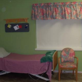 A simple hospital room with a single bed, green walls, and floral curtains.