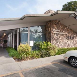 A modern building with a stone facade and an overhanging entrance, adjacent to a parking lot with a car.
