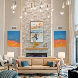 A modern living room with a high ceiling, featuring a central fireplace, colorful artwork, and elegant lighting.