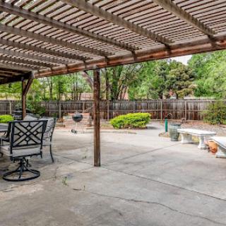 A serene outdoor patio space with a pergola, featuring seating and lush landscaping.