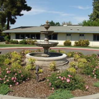 A beautiful garden featuring a fountain surrounded by flowers in front of a building.