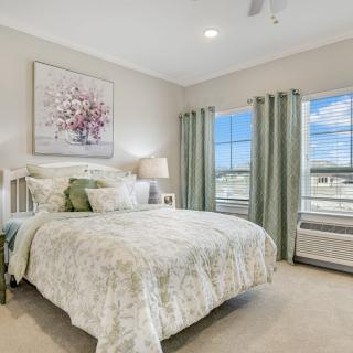 A beautifully decorated bedroom featuring a comfortable bed with floral bedding, soft lighting, and elegant curtains framing the windows.
