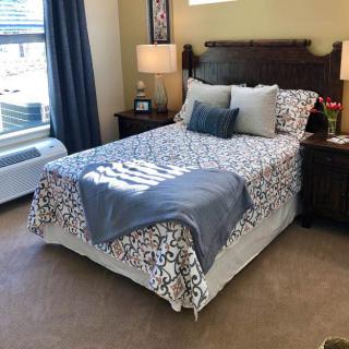 A cozy and well-lit bedroom with a neatly made bed and decorative pillows.