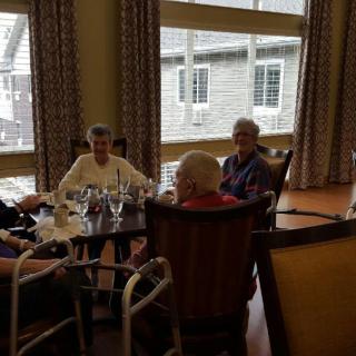 A group of seniors sitting together in a dining room, engaged in conversation.