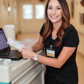 A cheerful nurse in black scrubs stands by a workstation, ready to assist patients.