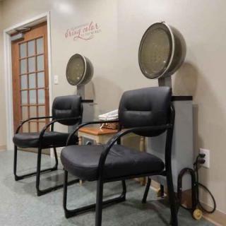 A salon waiting area featuring two chairs with attached hair dryers.