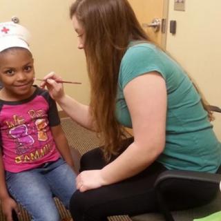 A child having her face painted by an artist during a fun indoor activity.