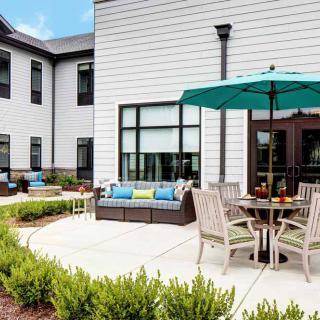 A modern patio with outdoor seating and an umbrella, surrounded by a well-maintained garden.