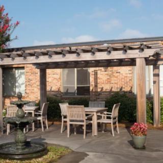 A patio with a pergola, outdoor seating area, and a fountain surrounded by flowers.