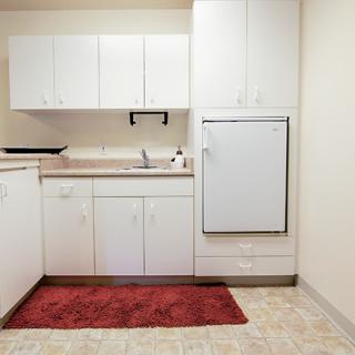 A minimalistic kitchen with white cabinets and a red rug on the floor.