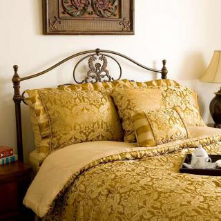 A cozy bedroom with ornate bedding and decorative pillows, featuring a metal headboard and a warm lamp on the bedside table.
