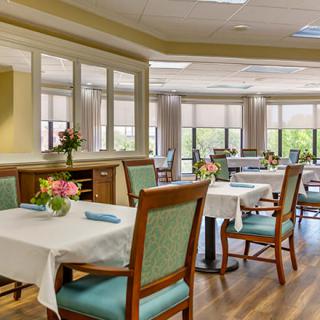 A well-lit dining room with neatly arranged tables and chairs, featuring elegant decor and large windows.