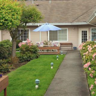 A neatly landscaped garden with a pathway, surrounded by flowers and featuring a patio with an umbrella.