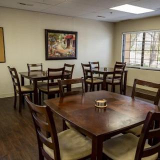 A cozy dining area with wooden tables and chairs, decorated with a wall painting and lit by natural light from the window.