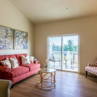 A cozy living room with a coral sofa, armchair, and artwork, featuring a sliding glass door leading to a balcony.