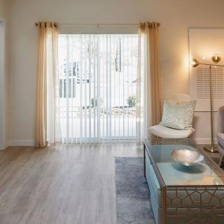 A bright and modern living room with minimalist decor, featuring a comfortable armchair, glass coffee table, and ample natural light streaming through sheer curtains.