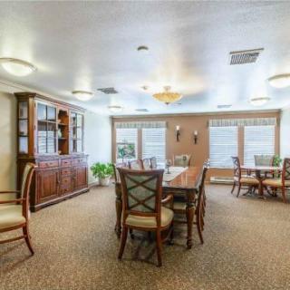 A spacious dining room with multiple tables and chairs, featuring large windows and warm lighting.