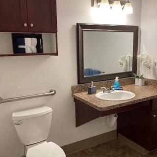 A clean and modern bathroom with a large mirror, sink, toilet, and wooden cabinets.