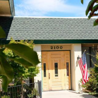A house entrance with a wooden door, adorned with an American flag and surrounded by greenery.