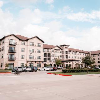 A suburban residential building with multiple stories and parked cars in front.