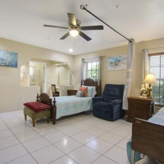 A spacious bedroom featuring a bed, armchair, and bedside lamp with tiled flooring.