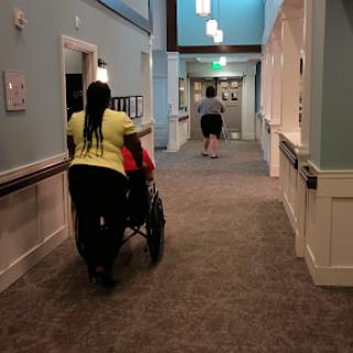 Two individuals walking in a brightly lit hallway, one pushing a stroller.