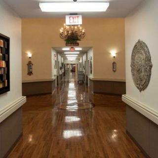 A well-lit hallway in a nursing home with wooden floors and decorative wall art.